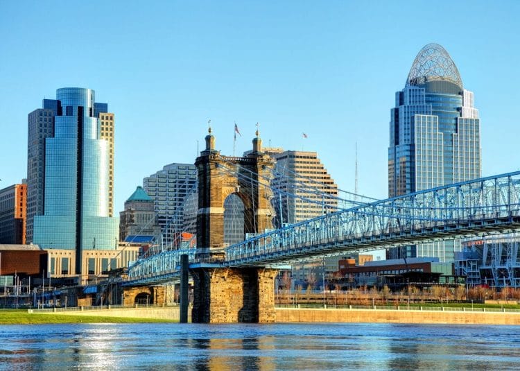 A large blue suspension bridge spans the river, framing a city skyline adorned with modern skyscrapers against a clear blue sky—a true feast for the senses.